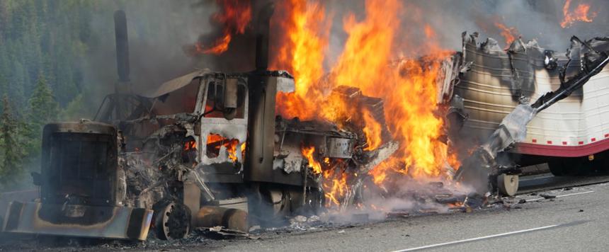 This image shows a semi-truck on fire on the side of the road.