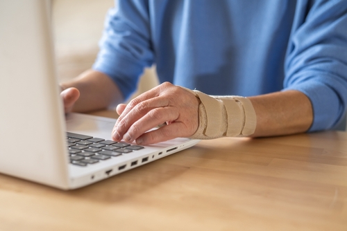 Woman wearing a wrist brace for carpal tunnel typing on a laptop representing clients seeking help from a repetitive stress injury lawyer.