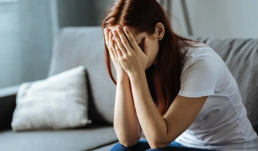 A young woman is sitting on the floor in front of a couch with her face buried in her hands depicting the grief and emotional devastation experienced by a family member seeking justice through a wrongful death attorney in North Carolina.