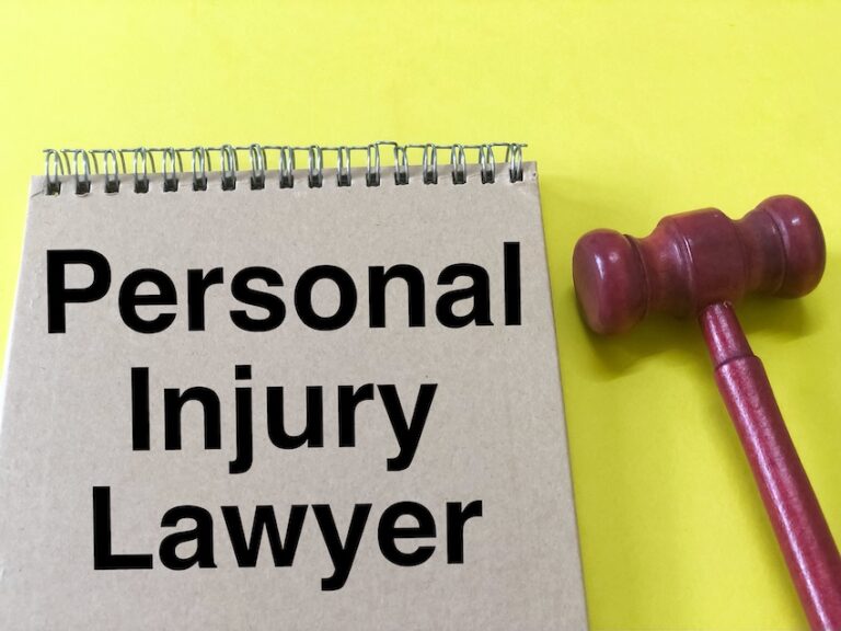 A spiral-bound notepad printed with the words "Personal Injury Lawyer" in bold black text sits beside a small wooden gavel on a bright yellow background directly identifying the legal professional injury victims should contact to protect their rights and pursue compensation in North Carolina.