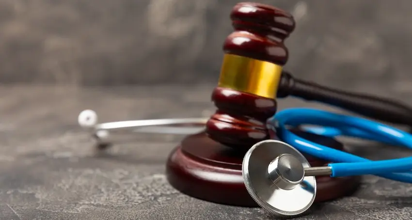 A polished wooden judge's gavel with a gold band rests on its sound block beside a blue stethoscope on a textured gray surface representing the intersection of medical evidence and legal advocacy that defines the work of a personal injury lawyer from 1 Charlotte Injury Lawyers in North Carolina.