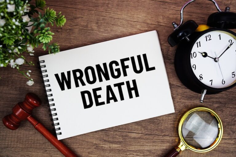A spiral notebook labeled Wrongful Death surrounded by a small gavel an alarm clock a magnifying glass and a potted plant on a wooden desk representing the time-sensitive legal process of filing a claim with a wrongful death attorney from 1 Charlotte Injury Lawyers.