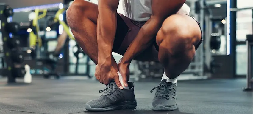 A grown man is holding his ankle in pain at the gym after a workout injury- illustrating when to contact a personal injury lawyer from 1 Charlotte Injury Lawyers for sports-related accidents in North Carolina.