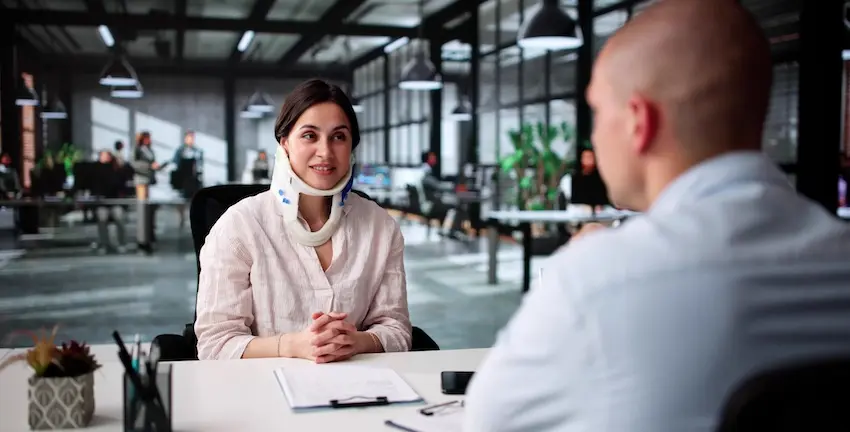 A woman is wearing a neck brace and is speaking with a lawyer during a consultation- showing how a personal injury lawyer helps injured clients discuss their case in North Carolina.