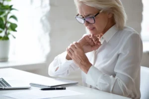 Woman writing at a desk and holding her wrist in pain from carpal tunnel consulting a repetitive stress injury lawyer for help.
